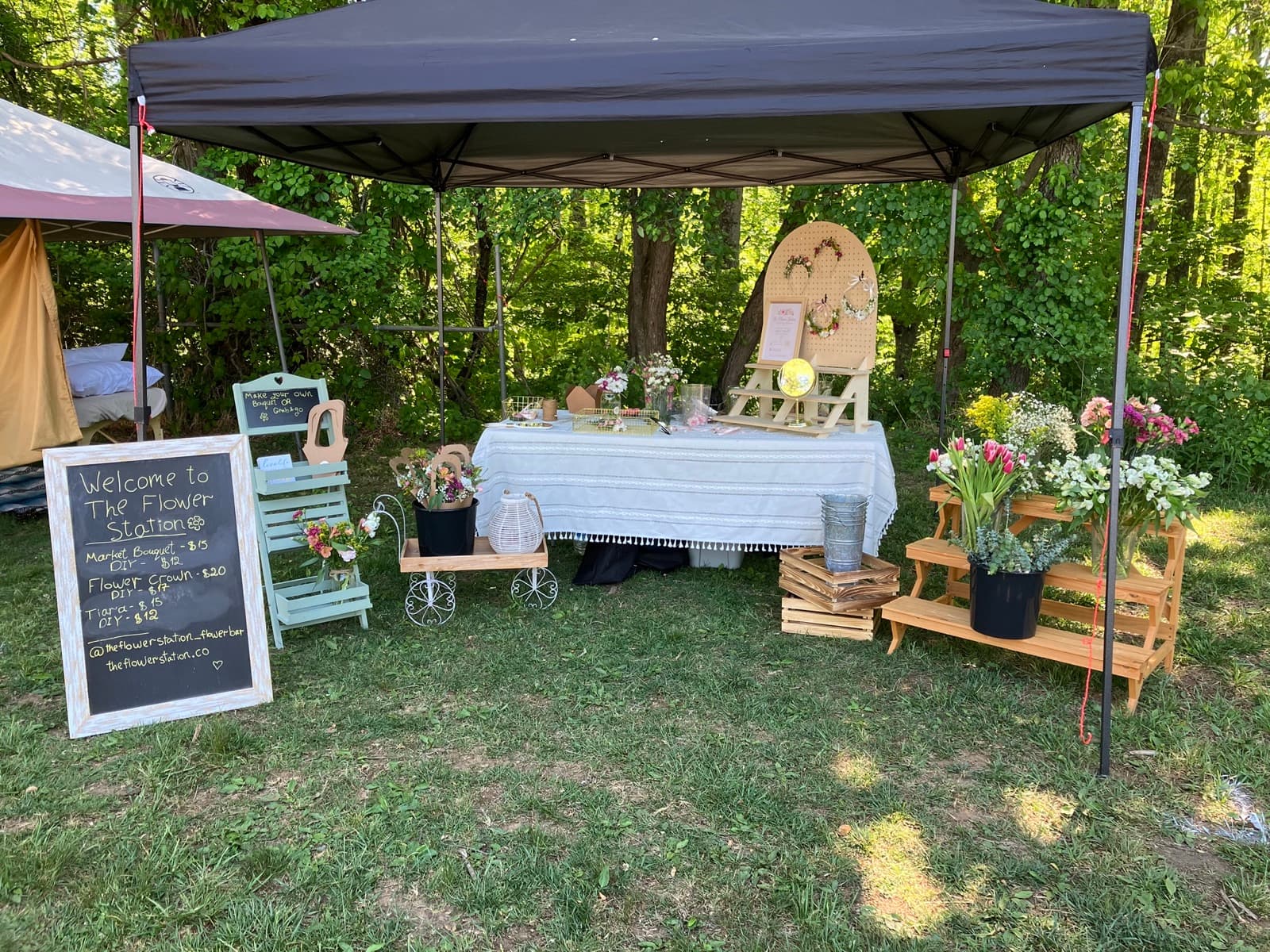 The Flower Station full outdoor booth setup at an Asheville event with welcome chalkboard and floral displays
